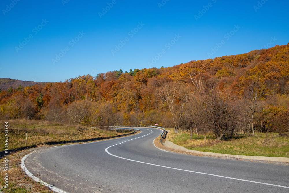 Landscape with a winding road on a hill in autumn, yellowed forest and blue sky Landscape with a winding road on a hill in autumn, yellowed forest and blue sky