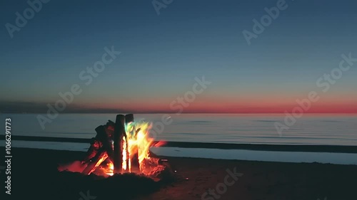 Colored Bonfire on the Beach against a Calm Sea or Ocean at Dark Romantic Evening - Slow Motion. Campfire Burning on Sand. Wood on Fire. Place for Bonfire. Fire Pit on Seaside. Fire for Signal
