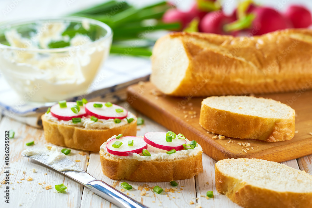 Appetizing crunchy baguette slices with cream cheese and radish slices and freshly chopped chives on a white wooden table. Appetizing crunchy baguette slices with cream cheese and radish slices and freshly chopped chives on a white wooden table.