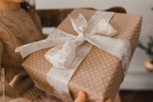 Close-up of a gift with a golden ribbon in kraft brown paper. Present for New Year, Christmas, holidays. A little girl with gift box.