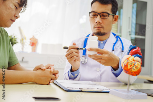 A doctor man sits at a desk in a hospital, explaining heart disease symptoms to a female patient. They discuss chest pain, palpitations, fatigue, dizziness, and the risks of myocardial ischemia photo