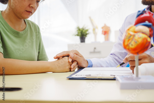 A doctor man sits at a desk in a hospital, explaining heart disease symptoms to a female patient. They discuss chest pain, palpitations, fatigue, dizziness, and the risks of myocardial ischemia photo