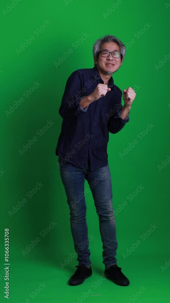 A vertical shot of a senior Asian man standing against a green background. A vertical shot of a senior Asian man standing against a green background.
