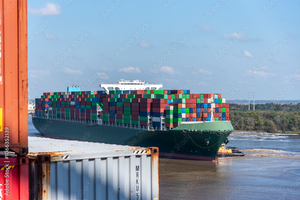 Naklejka premium A massive cargo ship loaded with containers maneuvers carefully during docking operations at the port of Charleston, USA.