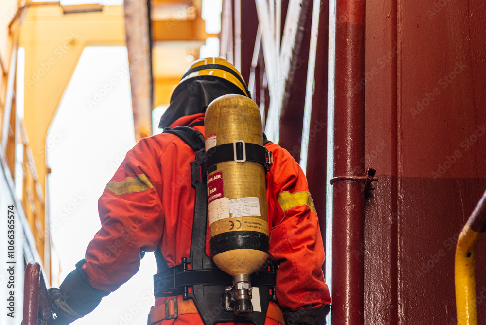 Fototapeta premium A firefighter in full protective gear, mask, and oxygen tank stands ready during a fire drill on board. Fully equipped, he executes fire suppression tasks with required precision.
