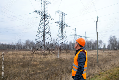 A man in a protective orange helmet and vest inspects power transmission line supports. Late autumn, bad weather