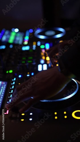 A DJ skillfully mixes music on a professional DJ console, illuminated by vibrant lights in a dimly lit nightclub. Neon lights and digital displays create a dynamic visual ambiance.