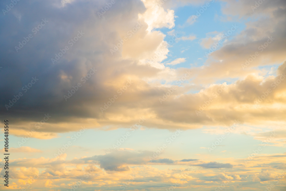 Fototapeta premium The sky is adorned with soft, fluffy clouds illuminated by warm golden light as day transitions into night, creating a peaceful atmosphere in the horizon.