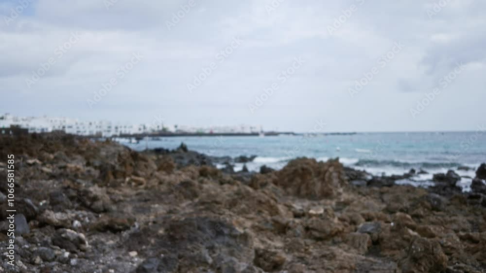 Blurred image of an outdoor rocky landscape with coastline and ocean view in lanzarote, canary islands, spain, featuring distant white buildings under a cloudy sky