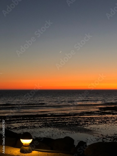 Anochecer costa andaluza, cielo arcoíris, cuarto de luna asomando tímida, horizonte naranja últimos rayos de sol, aguas mansas marea baja, contraste farola, fondo de pantalla cuadro marco photo