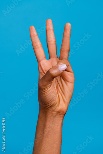 Vertical cropped closeup view of attractive girl hand showing three sign isolated over bright blue color background photo