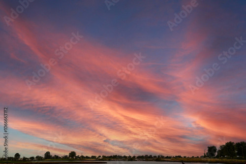 Golden twilight sky painted with hues of orange, pink, and red, where soft sunset clouds blend with dramatic storm shades. A breathtaking summer horizon glowing with evening light, capturing the beaut
