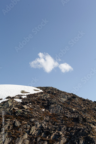 A lonely cloud hovering above a mountain with clear sky in the background.