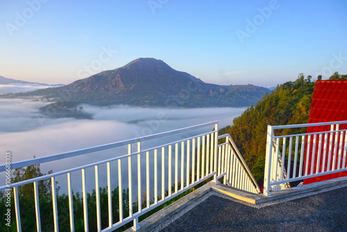 Sunrise view with fog and warm sunlight of the Bali mountains nature landscape of Mount Batur from the top of the house roof with stairs and white fence. Desa Pinggan, Kintaman, Bali, Indonesia. photo