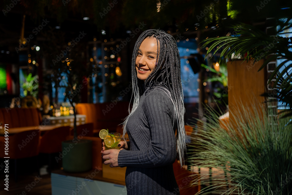young woman with afro braids is sitting in a coffee shop and drinking a cocktail young woman with afro braids is sitting in a coffee shop and drinking a cocktail