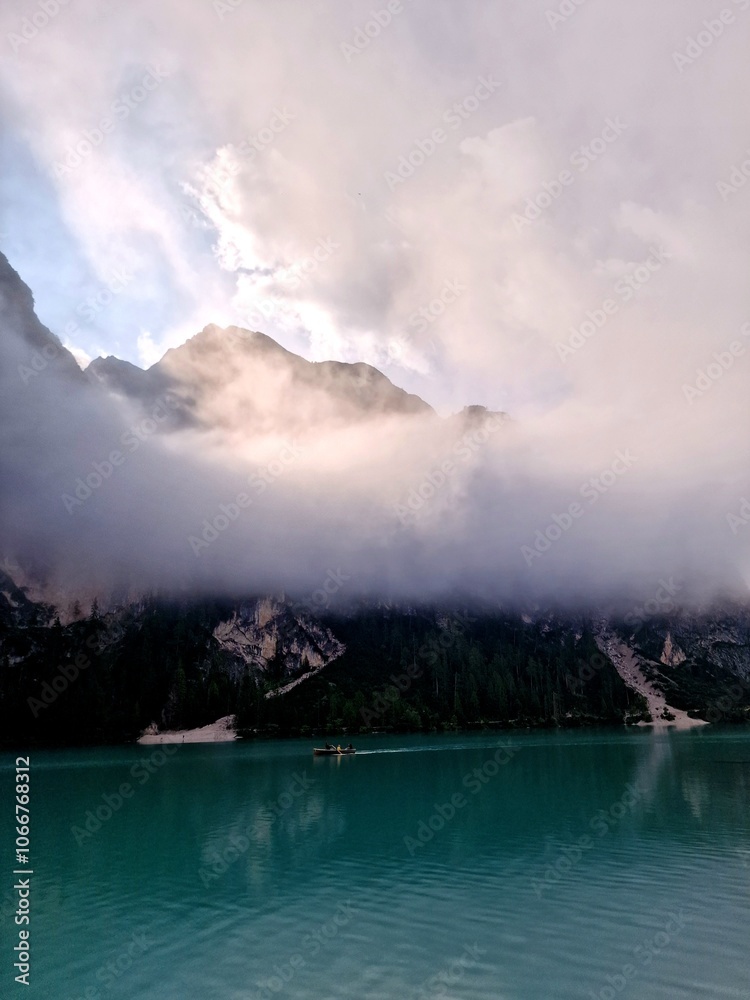 Serene turquoise lake and mountain peaks emerging through the clouds Serene turquoise lake and mountain peaks emerging through the clouds