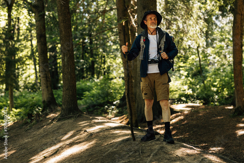 Full length of male in hiking clothes standing in a forest with a wooden stick and looking away photo