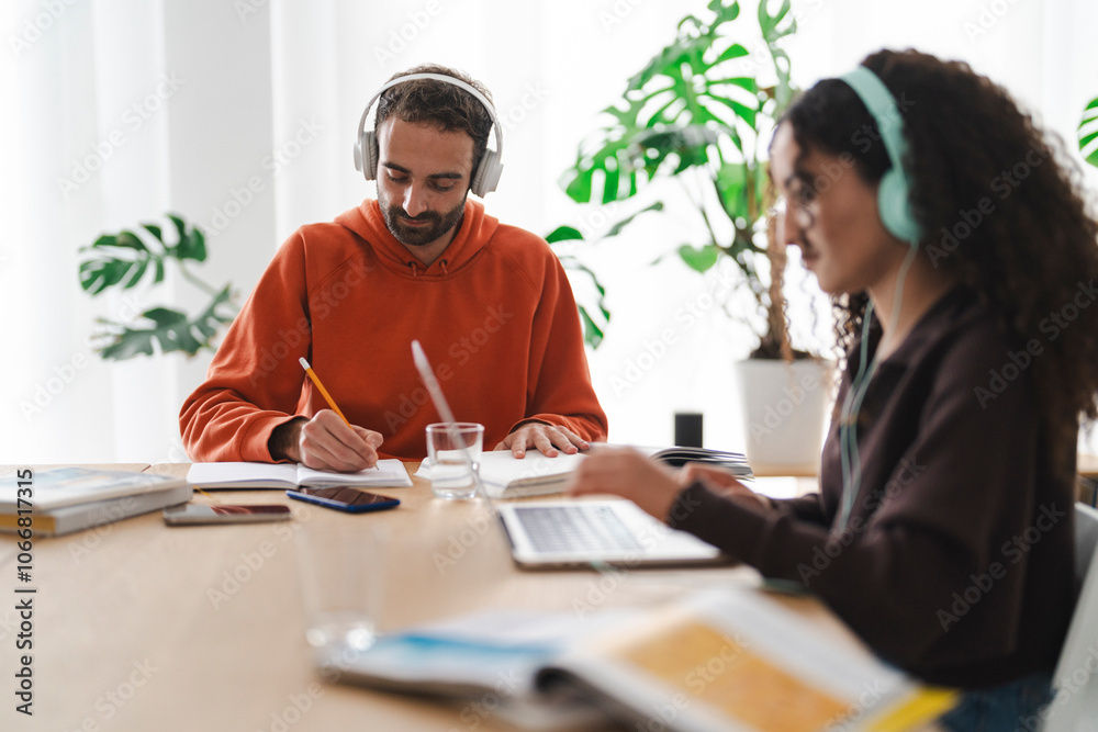 A coworker pair engrossed in their tasks, one taking notes with headphones on while the other types on a laptop, creating an atmosphere of focus and productivity. A coworker pair engrossed in their tasks, one taking notes with headphones on while the other types on a laptop, creating an atmosphere of focus and productivity.