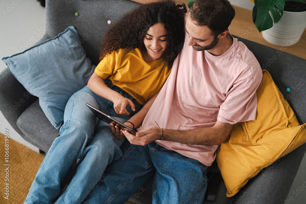 A relaxed couple sitting closely on a couch, engaged with a tablet, in a cozy living room adorned with indoor plants, creating a warm and welcoming atmosphere in a shared moment. A relaxed couple sitting closely on a couch, engaged with a tablet, in a cozy living room adorned with indoor plants, creating a warm and welcoming atmosphere in a shared moment.