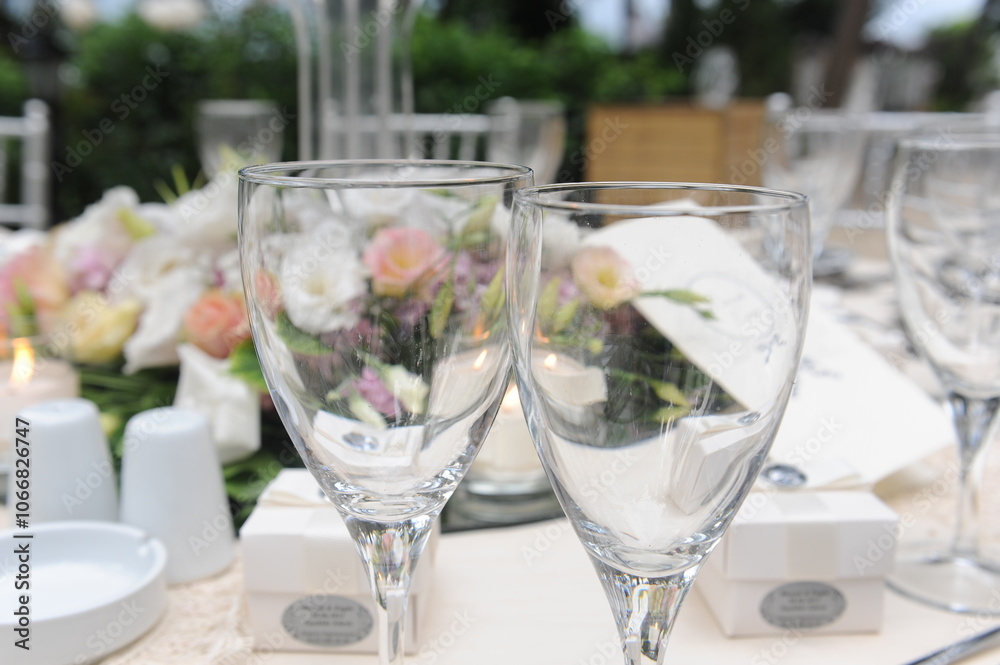 Elegant wedding table setting with wine glasses, floral centerpieces, and a soft white tablecloth in an outdoor garden ambiance. Perfect for wedding, celebration, or formal event themes Elegant wedding table setting with wine glasses, floral centerpieces, and a soft white tablecloth in an outdoor garden ambiance. Perfect for wedding, celebration, or formal event themes
