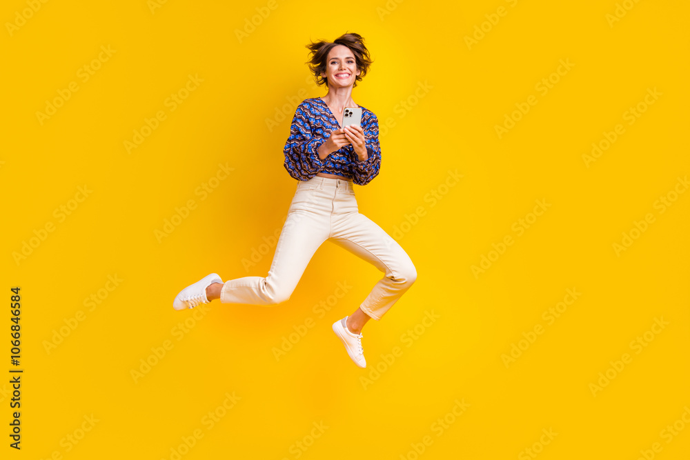 Full body size photo of young girl blogger jumping trampoline with smartphone social media enjoyer isolated on yellow color background Full body size photo of young girl blogger jumping trampoline with smartphone social media enjoyer isolated on yellow color background