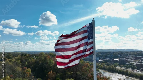 Patriotic American flag on flagpole moving over town.Sunny day in American city in fall season. Aerial close up orbit.Downtown with office buildings in background. Colored landscape of Connecticut. photo