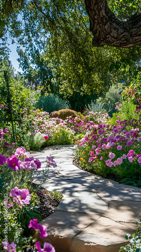 A winding stone path through a lush garden with pink flowers and a large tree.