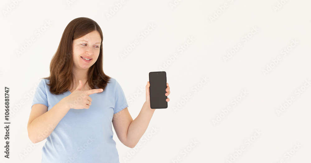 Close up portrait of a smiling woman showing and pointing at blank screen mobile phone while standing isolated over white background Close up portrait of a smiling woman showing and pointing at blank screen mobile phone while standing isolated over white background
