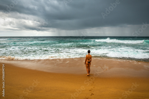 Tourist woman standing on the beach and looking on the stormy ocean