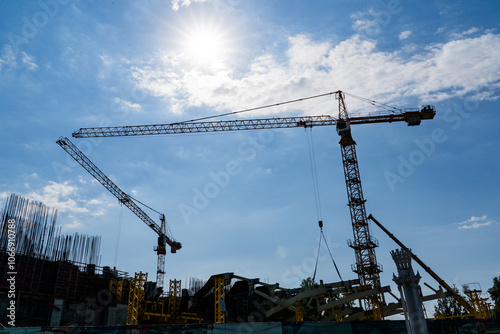 Silhouette of Construction Cranes Set Against a Bright Blue Sky During Daytime Hours