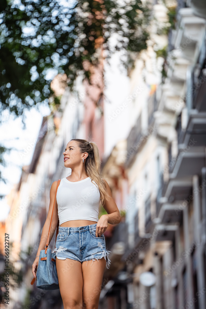 Young woman is walking down a city street during the day, holding a purse and smiling Young woman is walking down a city street during the day, holding a purse and smiling