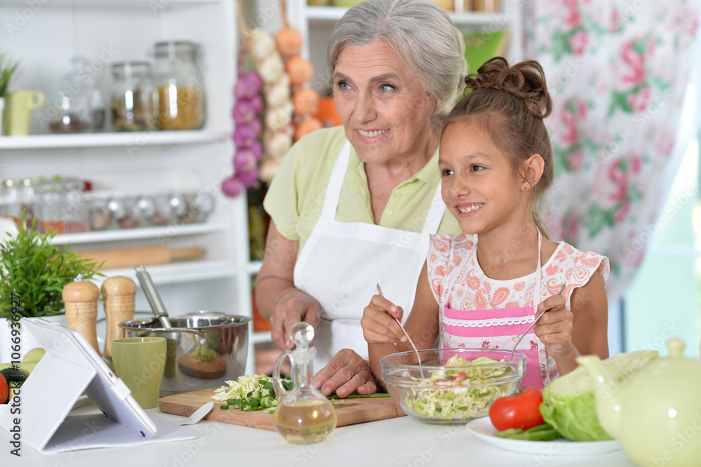 Grandmother with her granddaughter preparing a salad in the kitchen Grandmother with her granddaughter preparing a salad in the kitchen