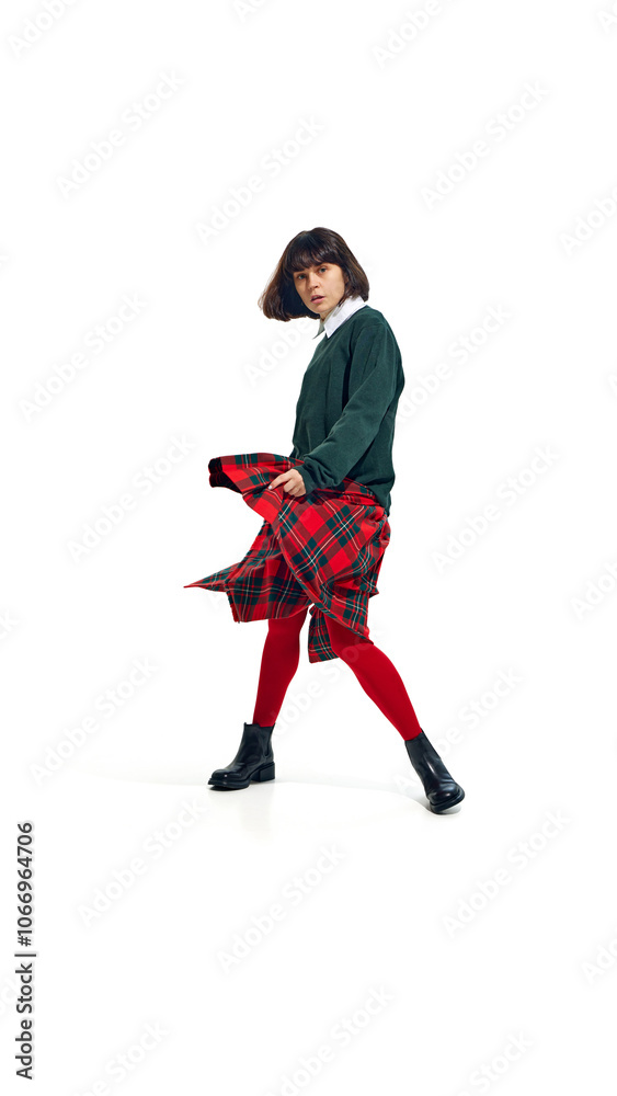Stylish woman wearing green sweater and red tights with plaid skirt, striking casual pose against white studio background. Concept of fashion and style, beauty, trendy,vibrant colors. Ad