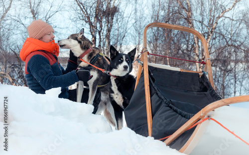 Man petting his husky sled dog in snowy wilderness during winter adventure travel, with sleigh in background, bond between man and dog, Finnish Arctic Circle, Tarvantovaara Wilderness Area, Finland photo