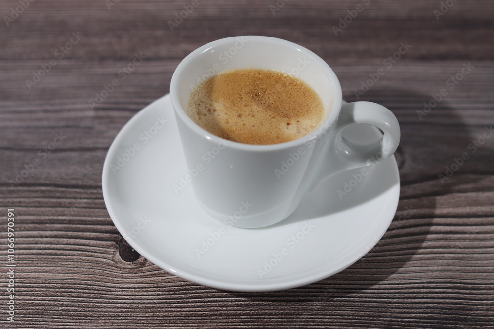 A white cup of espresso with its saucer on a wooden pattern. A white cup of espresso with its saucer on a wooden pattern.