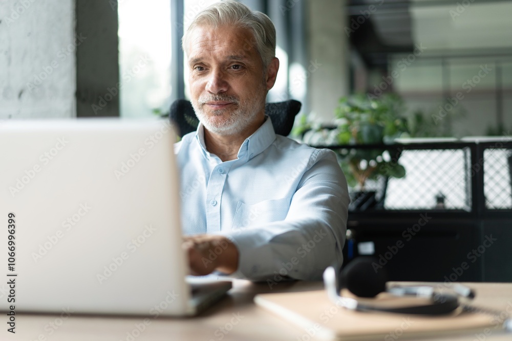 Mature 40s focused businessman, executive director working using laptop sitting at office Mature 40s focused businessman, executive director working using laptop sitting at office
