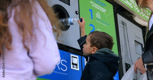 Toddler boy puts used plastic bottle into reverse vending machine on city street. Little child sorts trash to protect environment. Sustainable life photo