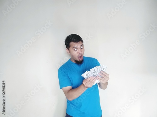 Asian adult man shows a shocked facial expression when he sees the US dollar bills he is holding photo