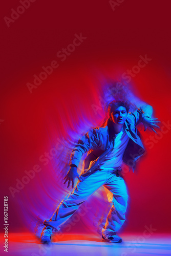 Creative design. Energetic performance of young man in casual clothes dancing hip hop, freestyle dance on red background with light wave effect. Concept of dance, art, modern style, youth culture photo