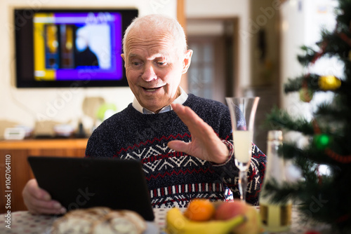 Elderly man wishes Merry Christmas by laptop to friends and acquaintances sitting at the festive table in house photo