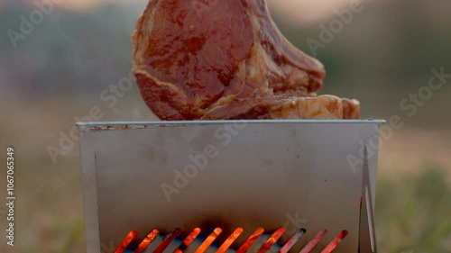 Pork chops steak grilled outdoors at camp. Grilled meat raw pork chops on portable grill depot with flames at campgrounds. Camping lifestyle concept. 