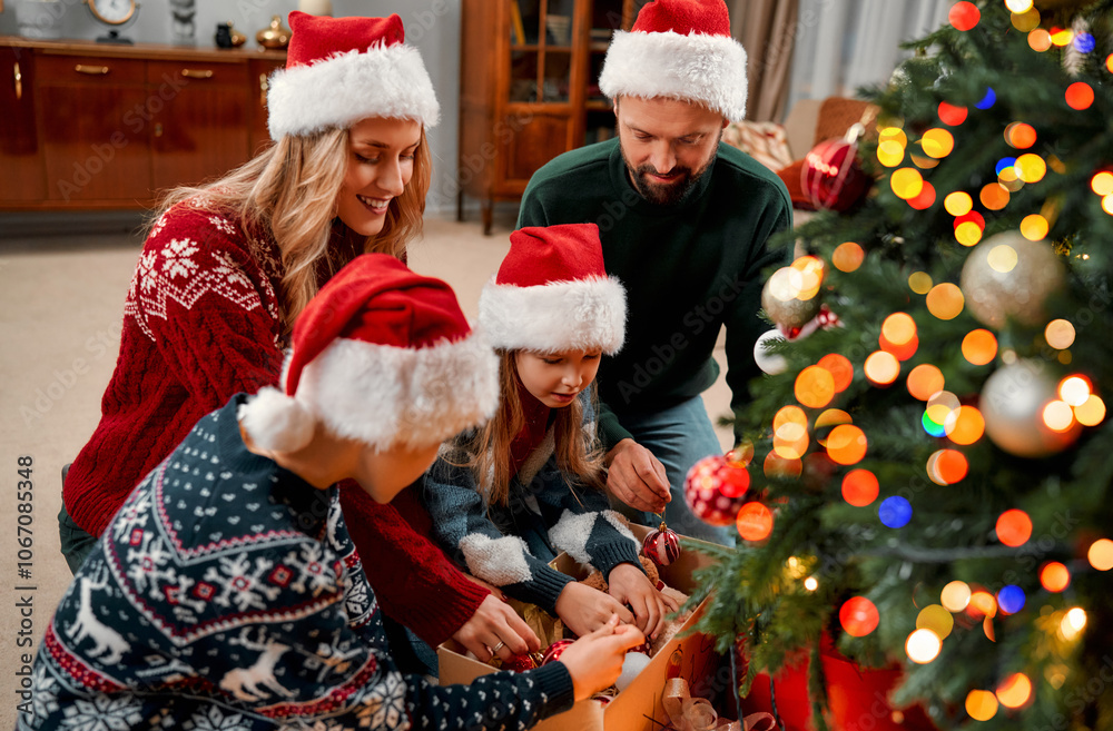 Happy family in festive sweaters and Santa hats having fun decorating the Christmas tree together at home. Family tradition. On the eve of Christmas. Happy family in festive sweaters and Santa hats having fun decorating the Christmas tree together at home. Family tradition. On the eve of Christmas.