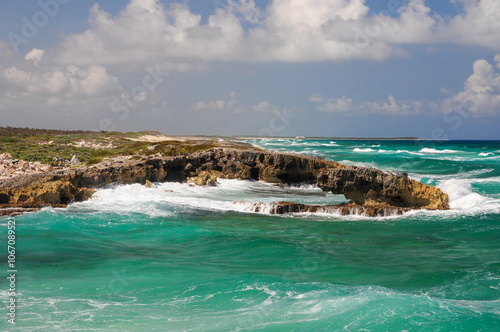 Turquoise waves crashing on rugged coast rocks under cloudy sky