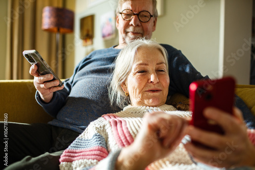 Senior couple relaxing on couch and using smartphones together photo