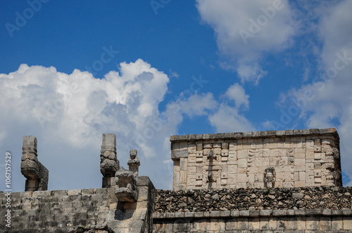 Ancient stone structures of Chichen Itza under a vibrant sky with clouds photo