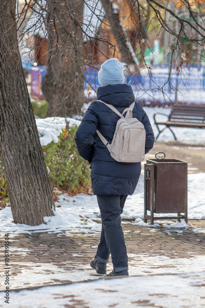 A woman wearing a blue coat and a blue hat is walking down a snowy sidewalk A woman wearing a blue coat and a blue hat is walking down a snowy sidewalk