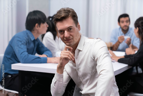 Confidence and happy smiling businessman portrait with background of his colleague and business team working in office. Office worker teamwork and positive workplace concept. Prudent