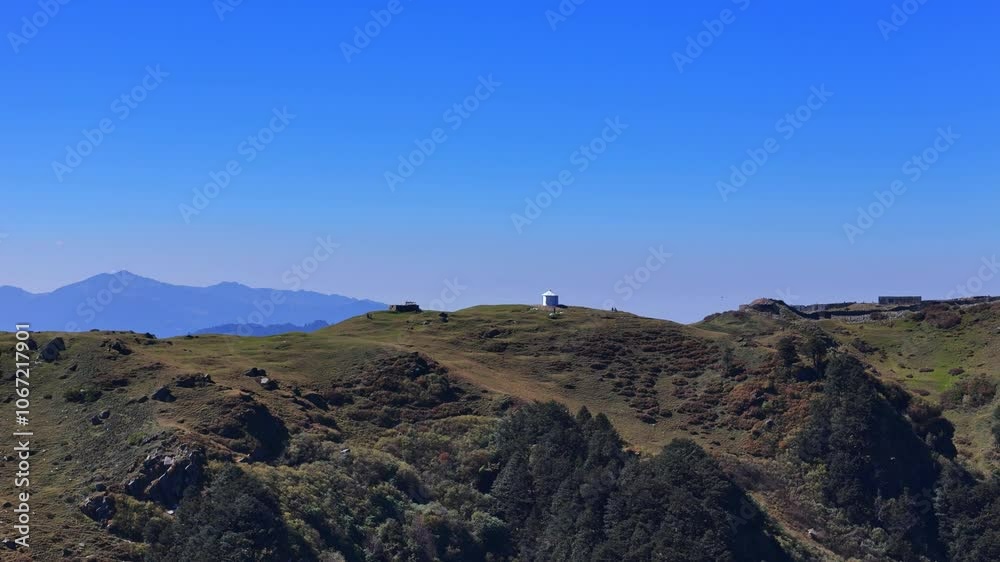 A mountain range adorned with vibrant green forests beneath a clear blue sky. A mountain range adorned with vibrant green forests beneath a clear blue sky.