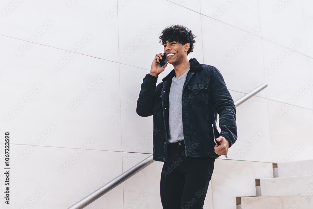 Trendy cheerful African American man speaking on phone while walking on urban staircase on street Trendy cheerful African American man speaking on phone while walking on urban staircase on street