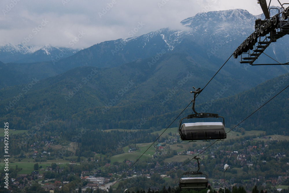 Obraz premium Ski Lift snowy mountain autumn forest with chair lift At The Ski Resort in Zakopane Poland. Holidays Vacation sport and outdoor activities tourism cable car empty seat grass field in green forest on